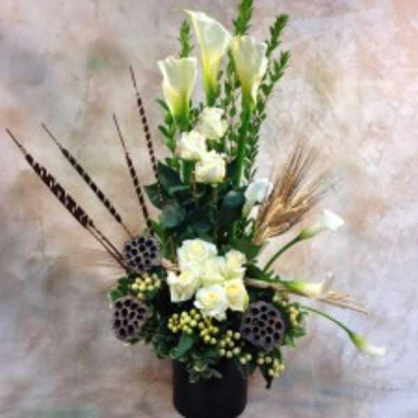 Tall white floral arrangement in a black vase with calla lilies and lotus pods