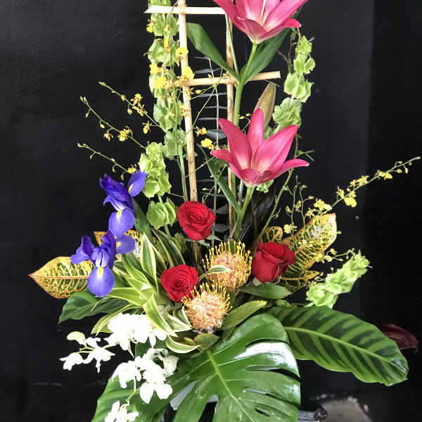 Tall tropical flower arrangement with pink lilies, red roses, and purple irises