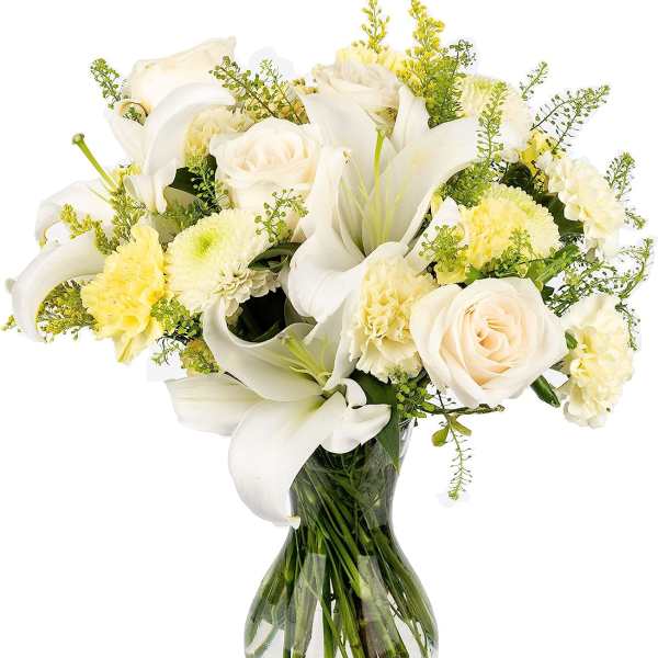 White lilies, cream roses, and pale yellow blooms arranged in a clear glass vase