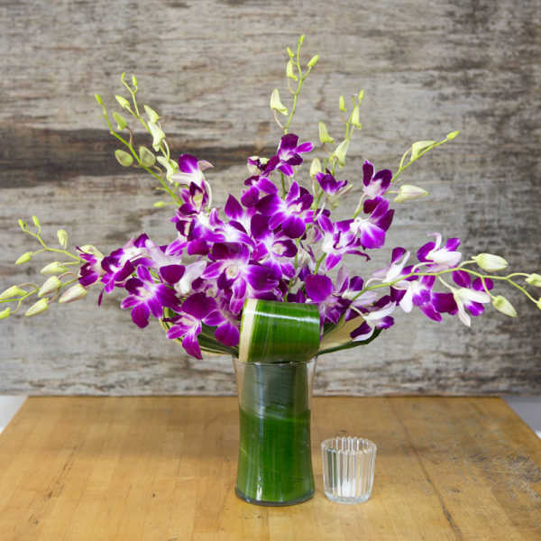 Purple and white orchids in a tall glass vase with a small candle holder beside it