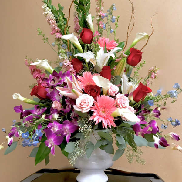 Large mixed bouquet of roses, lilies, orchids, and gerbera daisies in a white vase