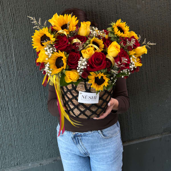 Large bouquet of red and yellow roses with sunflowers in a woven basket