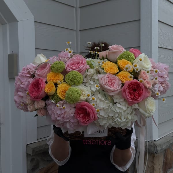 Large pastel bouquet with roses, hydrangeas, and small daisy accents in a basket