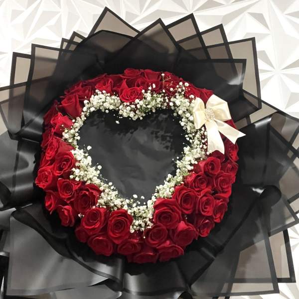Heart-shaped bouquet of red roses with white baby's breath and a cream ribbon