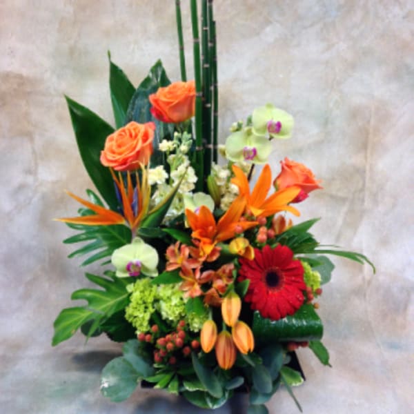 Tropical floral arrangement with orange roses, orchids, and a red gerbera daisy