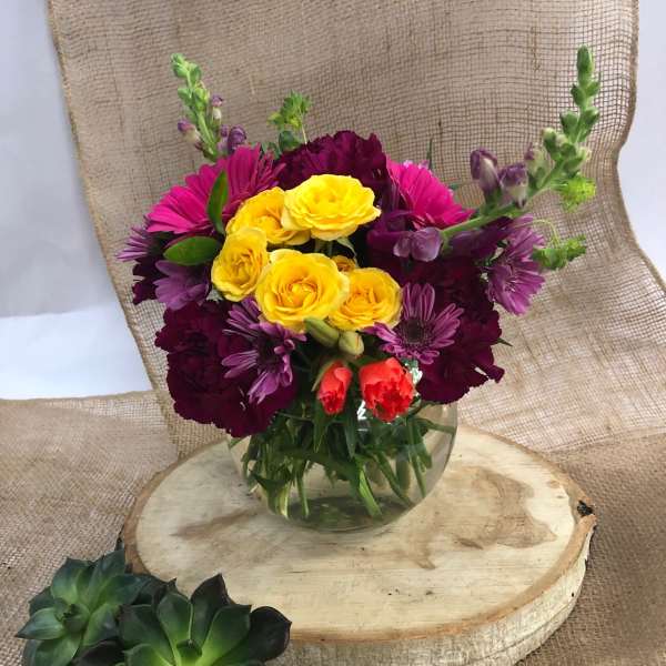 Mixed bouquet of yellow, pink, and purple flowers in a clear glass vase