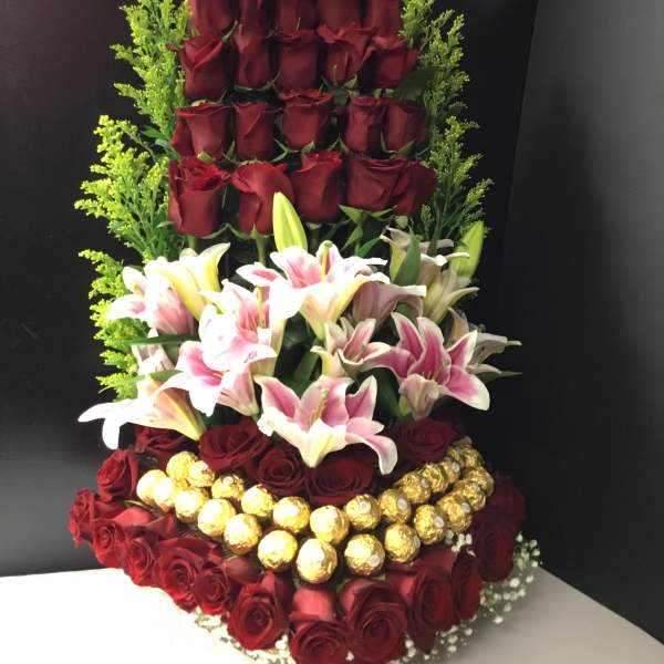 Tall arrangement of red roses, lilies, and gold-wrapped chocolates