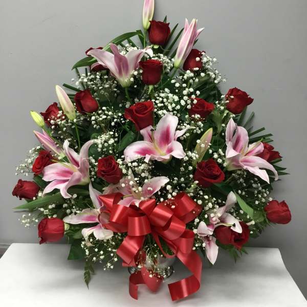 Red roses and pink lilies arranged with baby's breath and a red ribbon