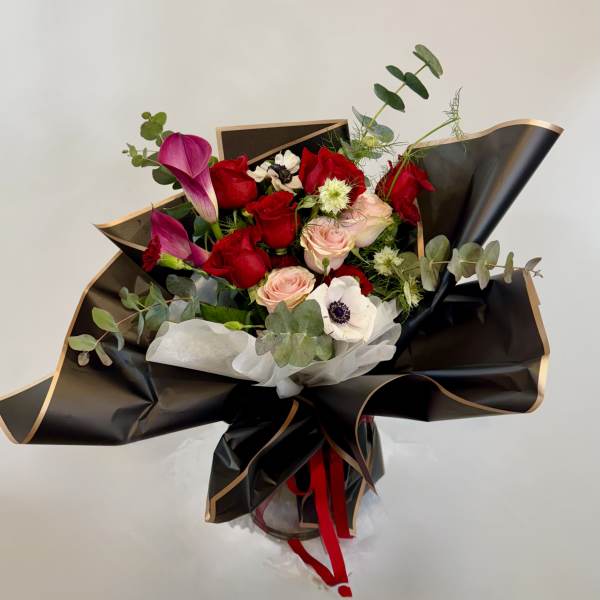 Bouquet of red and pink roses with purple calla lilies in black wrap