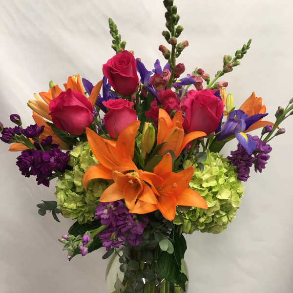Bright mixed bouquet with orange lilies, pink roses, purple flowers, and green hydrangeas in a glass vase