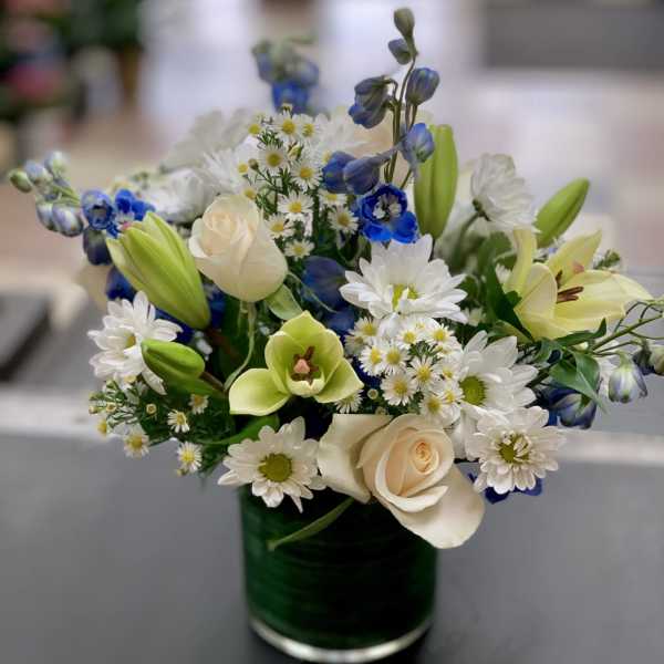 Bouquet of white daisies, cream roses, and blue flowers in a glass vase