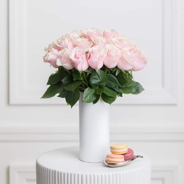 Pink roses arranged in a white vase with macarons beside it