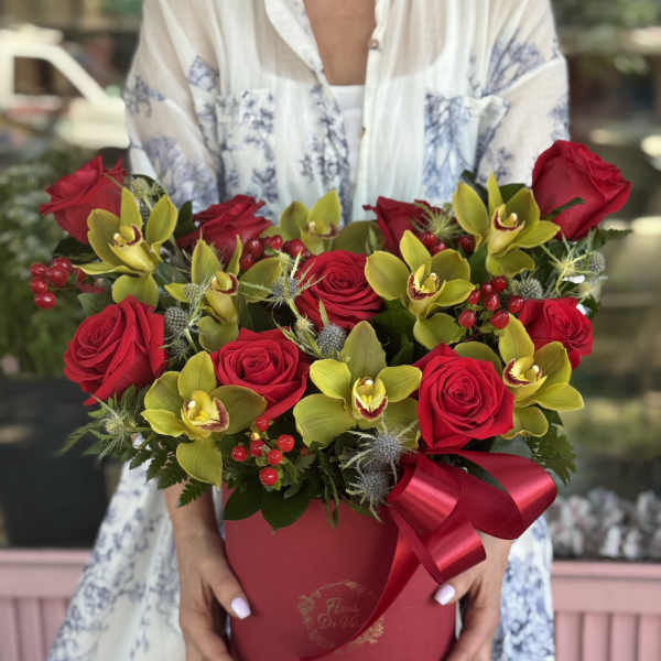 Red roses and yellow orchids arranged in a round red box with a ribbon