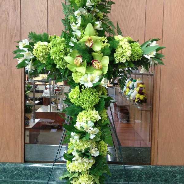 Tall green floral cross with white blooms on a stand