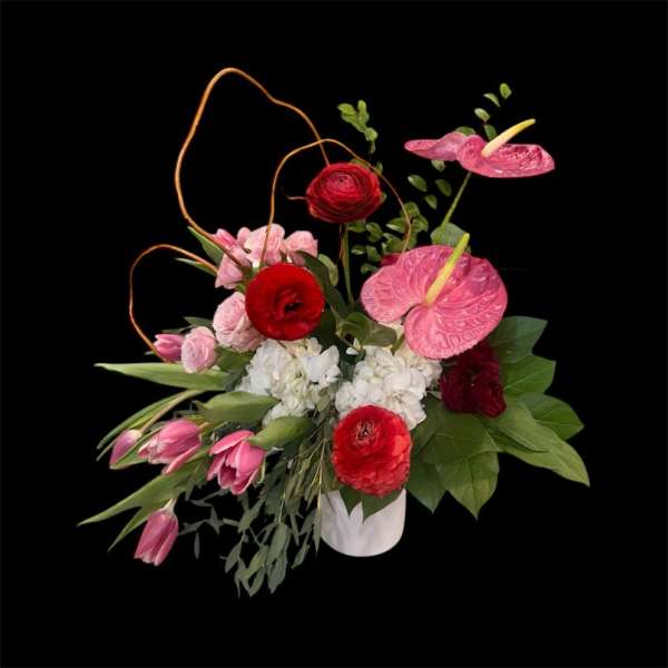 Pink and red floral arrangement in a white vase with tall curved stems