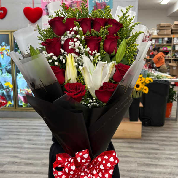 Tall wrapped bouquet of red roses and white lilies with a red heart-print bow