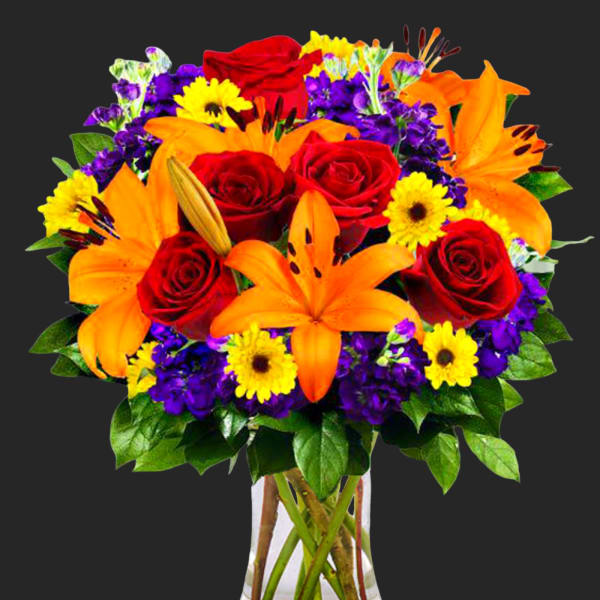 Bouquet of red roses, orange lilies, and yellow daisies in a clear vase