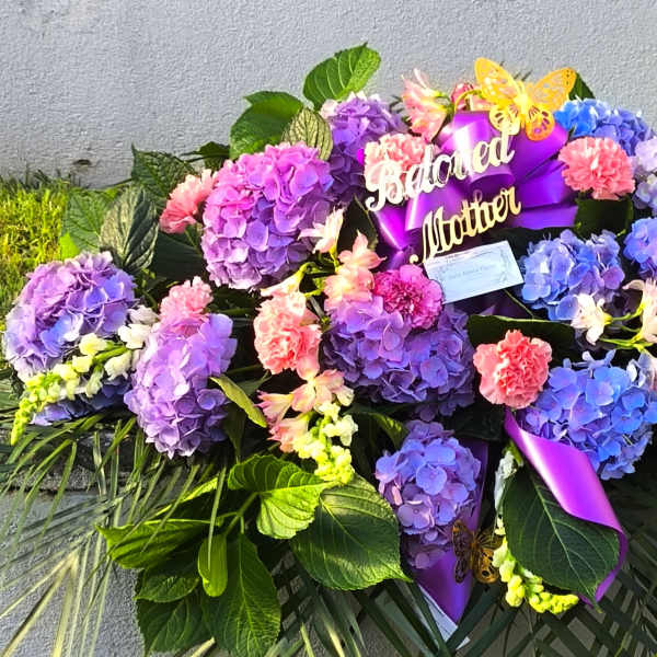 Large floral arrangement with purple hydrangeas, pink carnations, and a purple ribbon