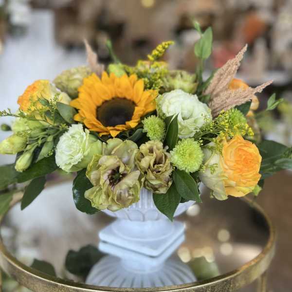Mixed floral arrangement with a sunflower in a white pedestal vase