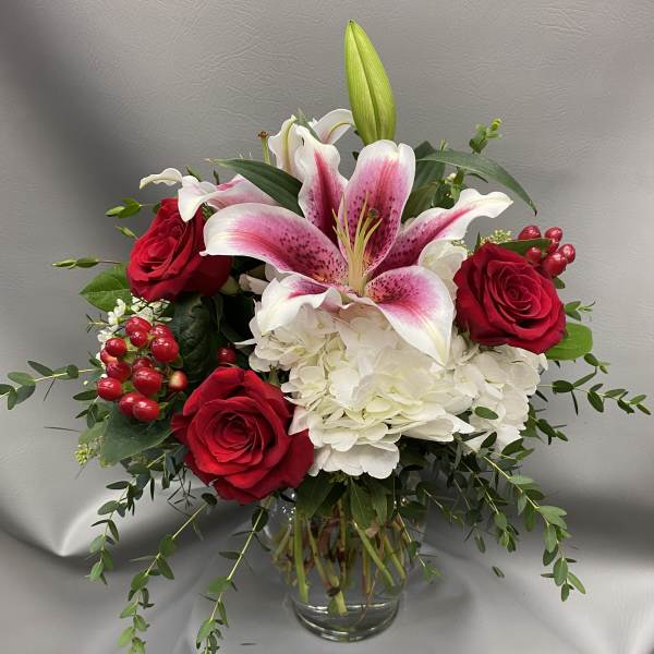 Red roses and white lilies in a glass vase with white hydrangea