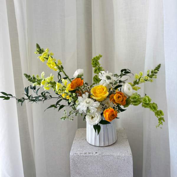 Yellow, white, and orange flowers in a white vase