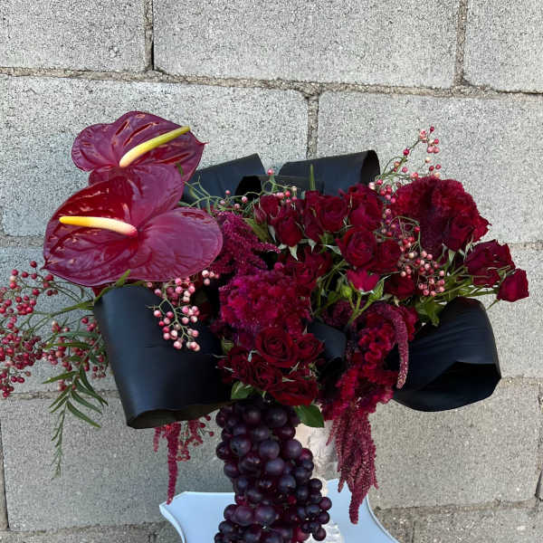 Deep red floral arrangement with anthuriums and roses in a white pedestal vase