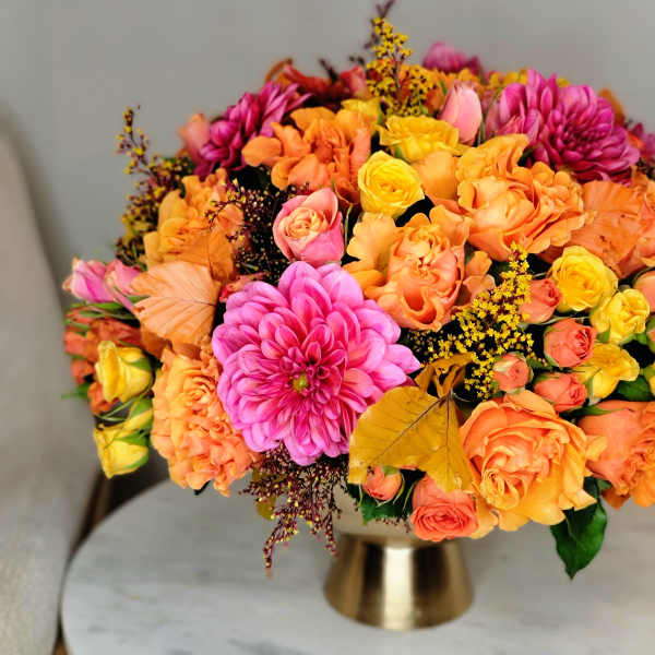 Bright mixed bouquet of orange, pink, and yellow flowers in a gold vase