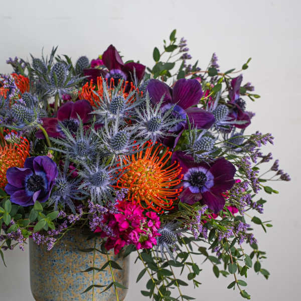 Colorful bouquet with purple blooms and orange pincushion flowers in a ceramic vase
