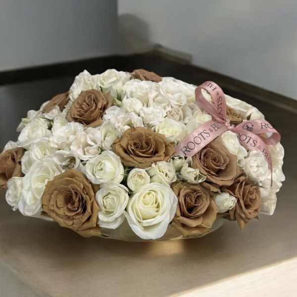 Round bouquet of white and tan roses tied with a pink ribbon