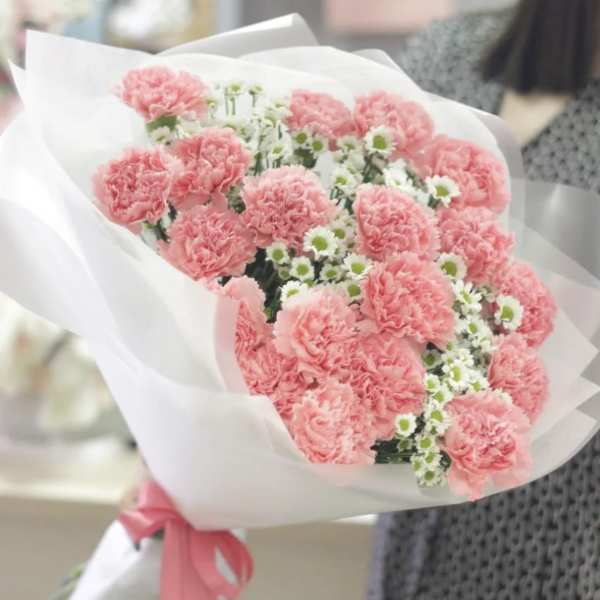 Pink carnations and small white daisies wrapped in white paper with a pink ribbon