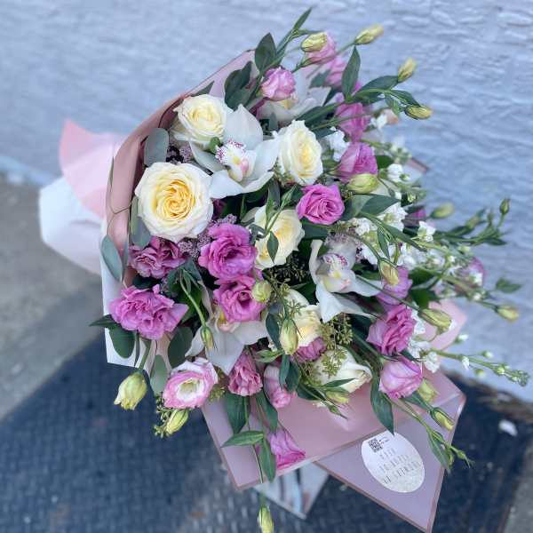 Bouquet of cream roses, pink lisianthus, and white orchids wrapped in pink paper