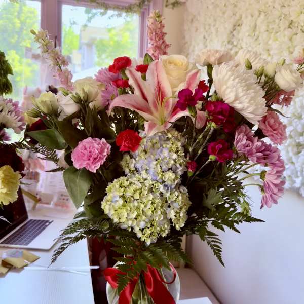 Mixed bouquet of pink and white flowers in a glass vase with a red ribbon