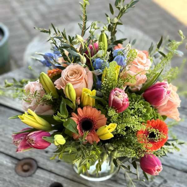 Mixed bouquet of roses, tulips, and gerbera daisies in a glass vase