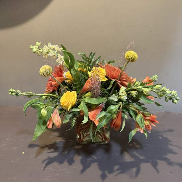 Mixed orange and yellow floral arrangement in a square glass vase