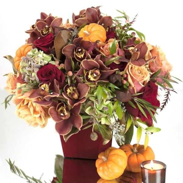 Autumn bouquet with orchids, roses, and small pumpkins in a red vase