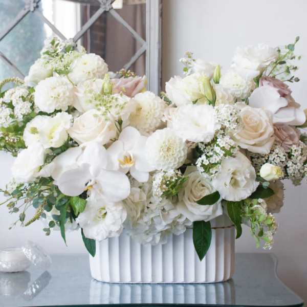 White floral arrangement in a ribbed white vase with pale pink accents