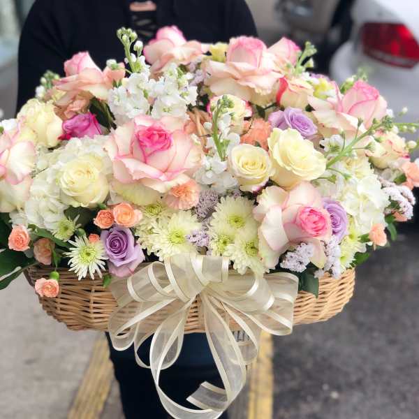 Basket of pastel roses, daisies, and small filler flowers with a ribbon bow