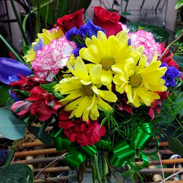 Mixed bouquet with yellow daisies, red roses, and pink carnations in a glass vase