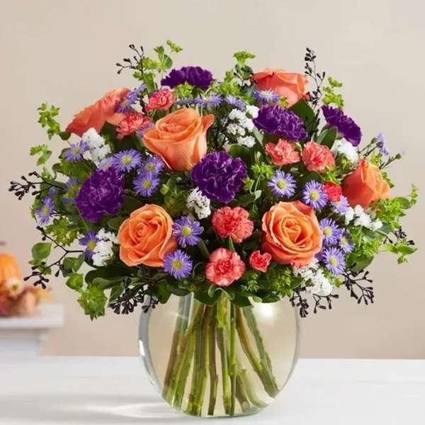 Bouquet of orange roses, purple flowers, and pink carnations in a glass vase