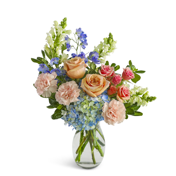 Peach roses, pink carnations, blue hydrangeas, and delphinium in a clear glass vase