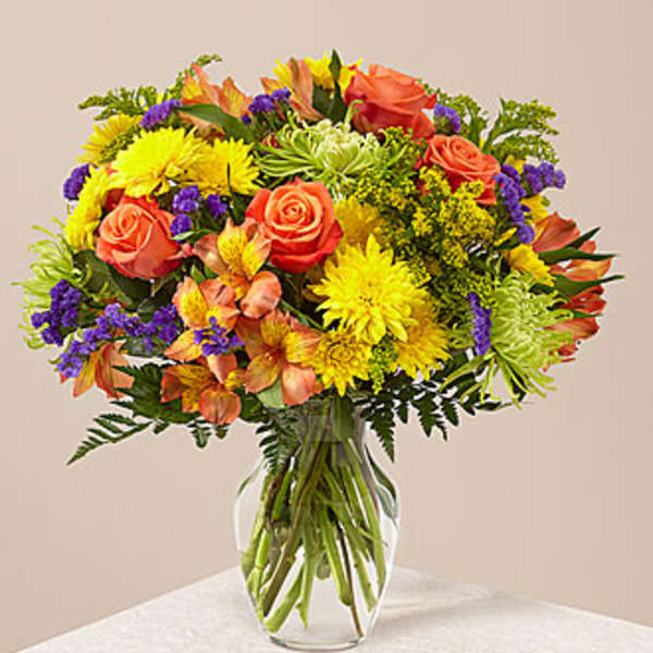 Mixed bouquet of roses, chrysanthemums, and purple filler in a glass vase
