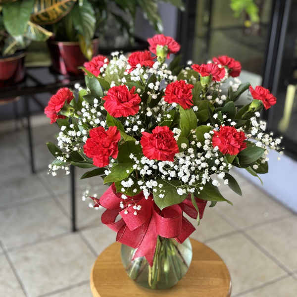 Red carnations and baby's breath in a glass vase with a red ribbon