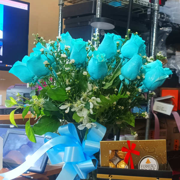 Blue roses in a glass vase with a ribbon and chocolates in a gift bag