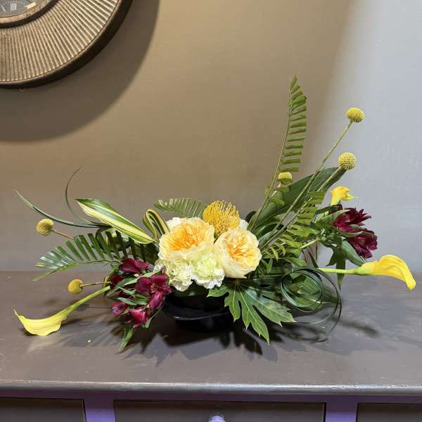 Low floral arrangement with yellow calla lilies and burgundy blooms in a black bowl