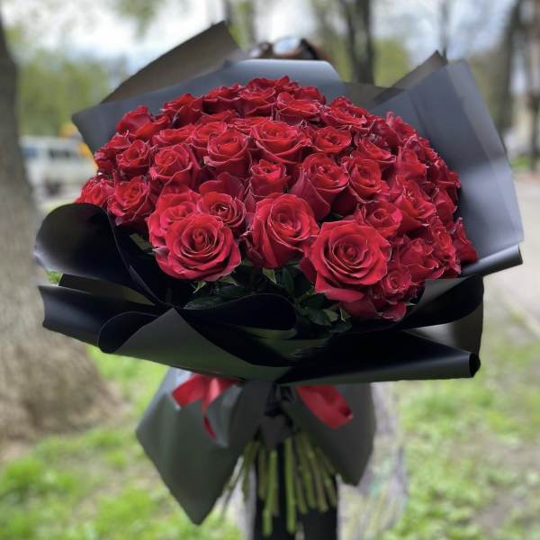 Large bouquet of red roses wrapped in black paper with a red ribbon