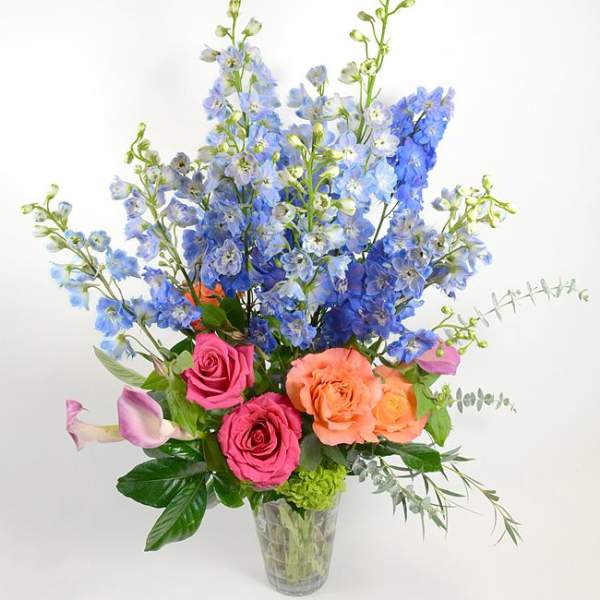 Tall bouquet of blue flowers with pink and peach roses in a clear vase