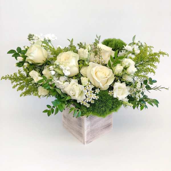 Cream roses and white blooms in a square vase with green accents