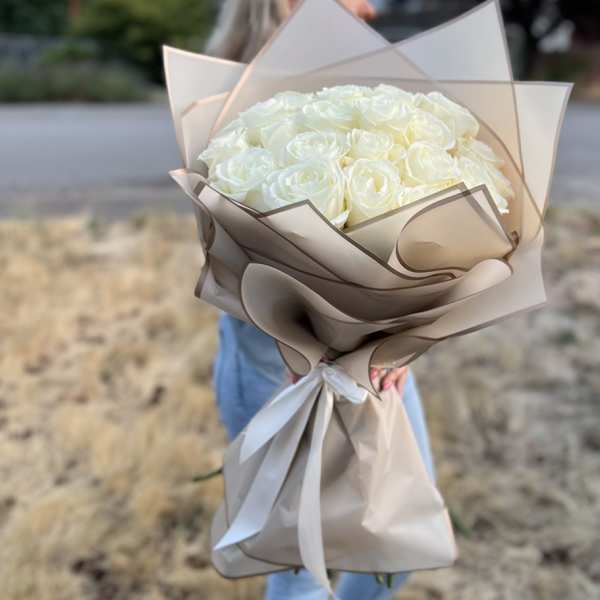 Bouquet of white roses wrapped in beige paper with a white ribbon
