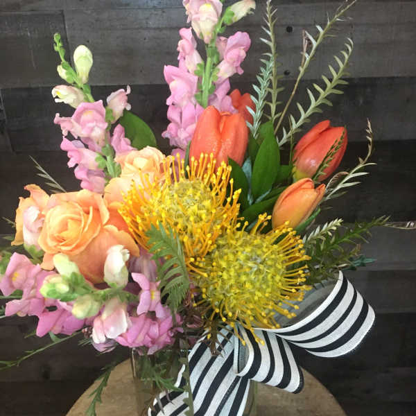 Bouquet of pink snapdragons, orange roses, and yellow pincushion protea in a glass vase