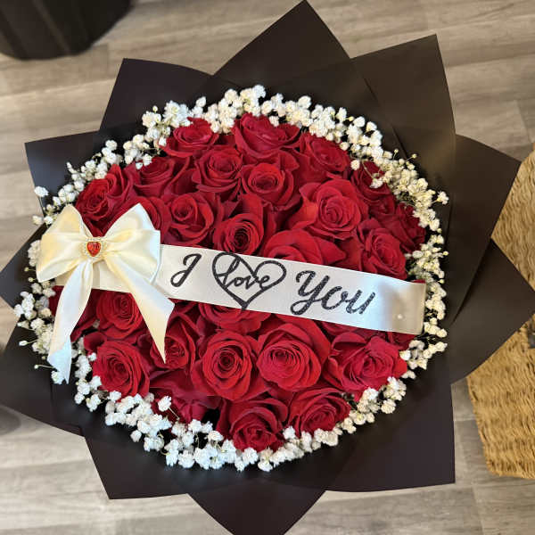 Round bouquet of red roses with a white ribbon and "I Love You" band